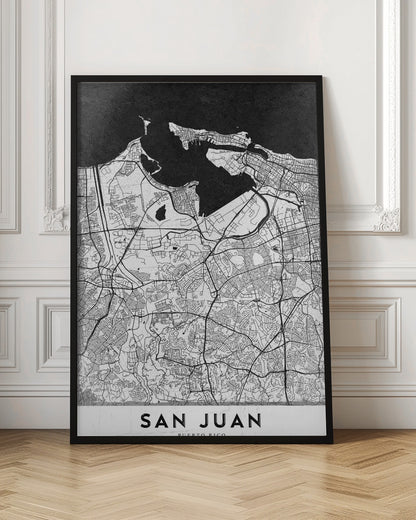 A minimalist black and white map of San Juan, Puerto Rico, shown as a framed poster. The land is depicted in white with intricate black lines for roads and streets, while the surrounding water is a solid, textured black. A white banner at the bottom features the text 'SAN JUAN' in a bold, black, sans-serif font. Artwork