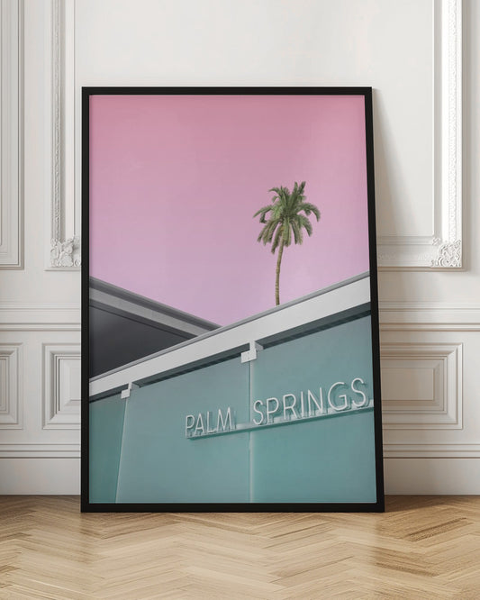 A low-angle shot of a modern building with a frosted teal glass facade and a white neon sign that reads 'PALM SPRINGS'. Above the building, a single tall palm tree stands against a solid, vibrant pink sky, creating a minimalist and stylized composition. Decor