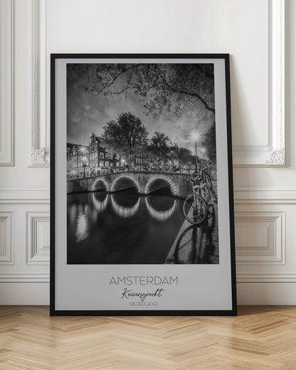 A black and white poster of Amsterdam's Keizersgracht canal at night. An arched bridge with glowing lights is the centerpiece, its reflection shimmering on the dark water. Bicycles are parked along the bridge and in the foreground on a cobblestone path. Classic canal houses and trees line the background under a dramatic, cloudy sky. The image is framed with text below reading 'AMSTERDAM Keizersgracht NEDERLAND'. Artwork