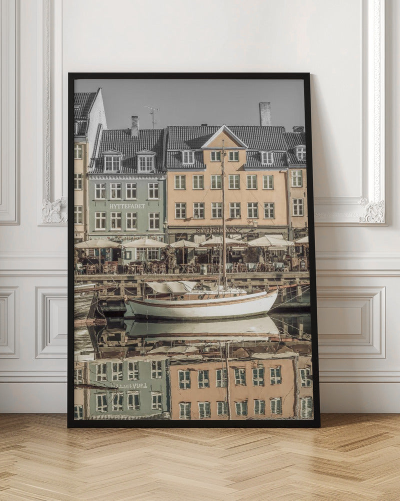 A scenic photograph of a European harbor with colorful buildings reflected in the water. A white sailboat is moored in the foreground in front of a pale green and a yellow gabled building. The image has a selective color effect, with the building facades in muted tones and the sky and roofs in black and white. Artwork