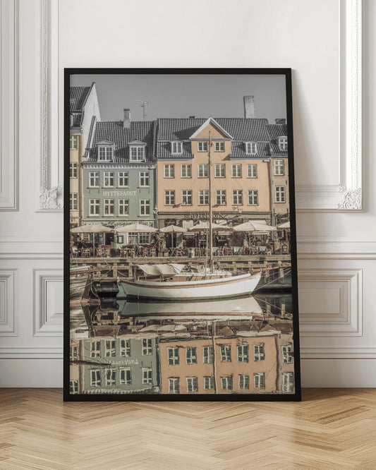 A scenic photograph of a European harbor with colorful buildings reflected in the water. A white sailboat is moored in the foreground in front of a pale green and a yellow gabled building. The image has a selective color effect, with the building facades in muted tones and the sky and roofs in black and white. Artwork