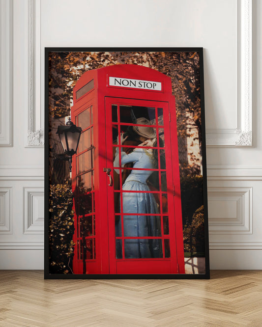 A couple in vintage clothing share a passionate kiss inside a classic bright red telephone booth. The woman is wearing a light blue dress, and the man wears a hat. The sign above the booth door reads 'NON STOP'. The setting appears to be outdoors in autumn. Wall Art