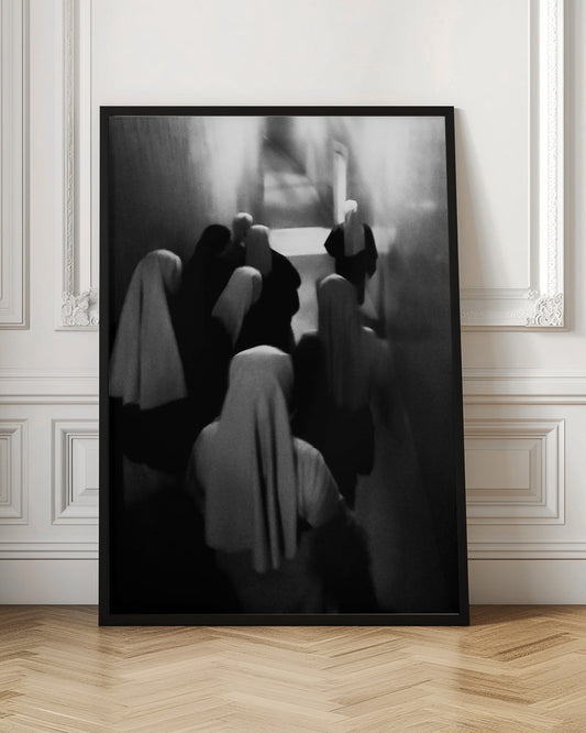 A mysterious black and white photograph captures a group of robed figures, possibly nuns, from above as they walk down a dark, narrow corridor. The image is blurred, creating a ghostly, ethereal atmosphere as the figures' white head coverings stand out against the deep shadows. Artwork