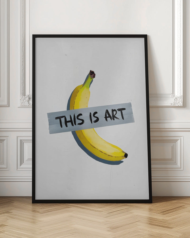 A framed artwork depicting a single yellow banana taped to a white wall with a grey strip of tape that reads 'THIS IS ART' in black marker-style font. Artwork