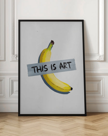A framed artwork depicting a single yellow banana taped to a white wall with a grey strip of tape that reads 'THIS IS ART' in black marker-style font. Artwork