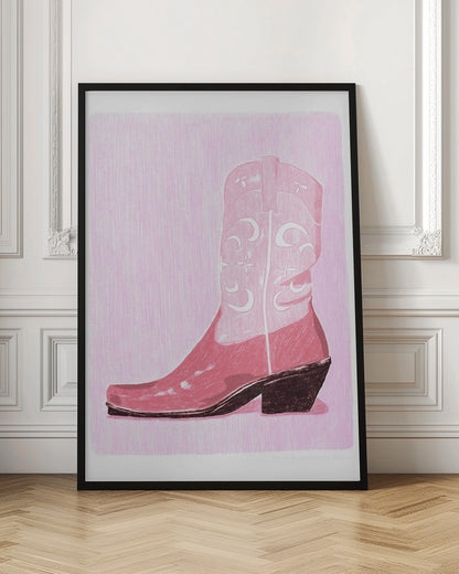 A framed art print of a pink cowboy boot against a light pink, textured background. The boot is illustrated in a block-print style with shades of pink, white decorative inlay patterns of moons and stars, and a dark brown heel and sole. Decor