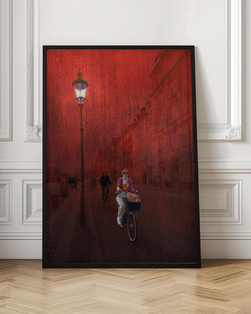 A surreal artistic image of a city street bathed in a textured red light. A woman rides a bicycle with a basket towards the viewer, while another cyclist is in the background. A tall, ornate lamppost is lit on the left side of the cobblestone street. Wall Art