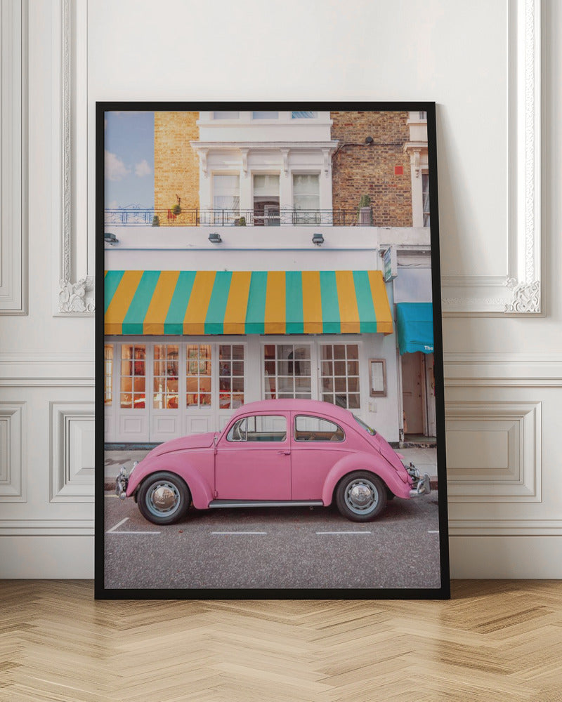 A vibrant, eye-level photograph of a vintage pink Volkswagen Beetle parked on a city street in front of a charming white storefront with a bold yellow and teal striped awning. Wall Art