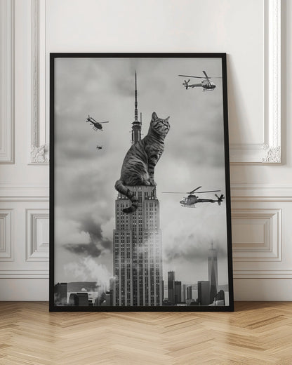 A surreal black and white image depicting a giant tabby cat sitting on top of the Empire State Building, similar to King Kong. Helicopters fly around the colossal cat against a cloudy New York City skyline. Decor