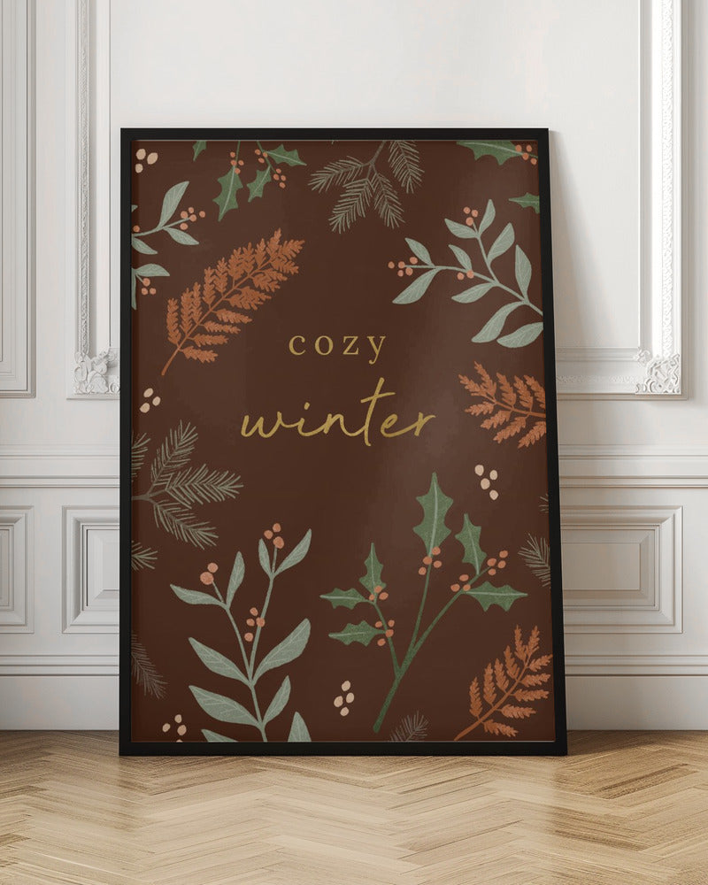A warm, illustrative poster with a dark brown background featuring the words 'cozy winter' in gold script at the center. The text is framed by a wreath of winter botanicals, including holly, pine needles, and ferns in shades of green and burnt orange. Print