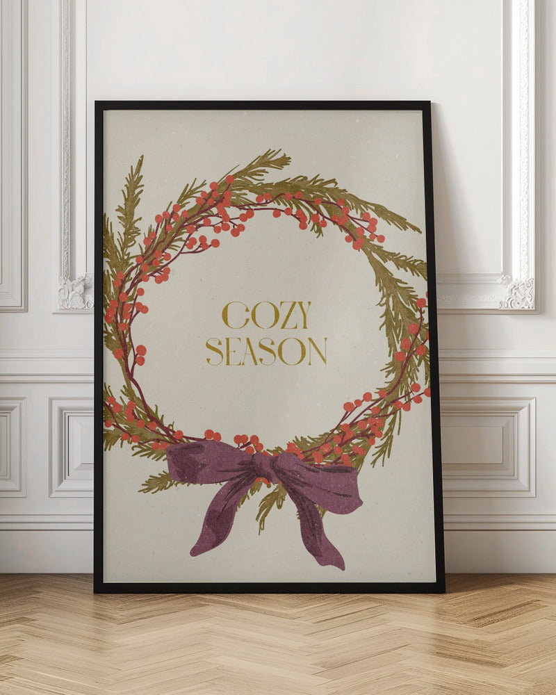A vintage-style illustration of a festive wreath made of green boughs and red berries, tied with a large purple bow at the bottom. The text 'COZY SEASON' is written in gold inside the wreath on a cream-colored background, all enclosed in a thin black frame. Wall Art