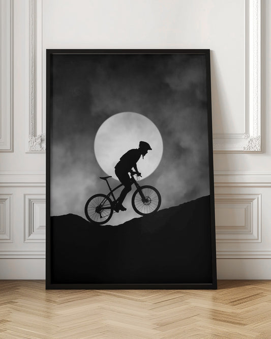A dramatic black and white silhouette of a mountain biker riding uphill against the backdrop of a large, full moon in a cloudy night sky. Decor