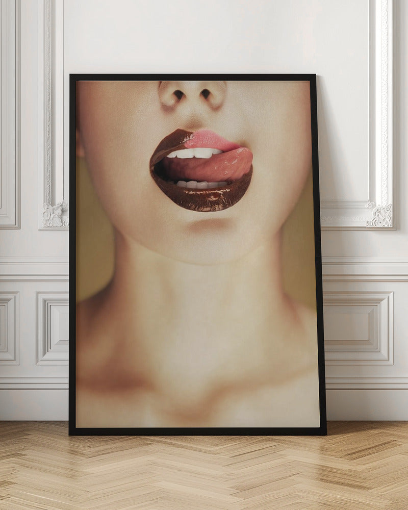 A close-up photograph of a woman's mouth with two-toned lipstick. The lips are mostly covered in glossy dark brown, with the upper right section in light pink. Her tongue is out, licking the pink part of her lip, revealing her white teeth. Print