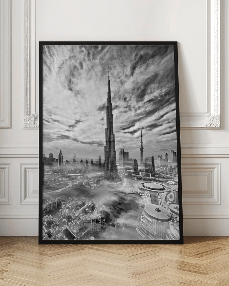 A dramatic black and white high-angle photograph of the Burj Khalifa dominating the Dubai cityscape, with swirling clouds above and a light mist surrounding the buildings below, all enclosed in a black frame. Poster