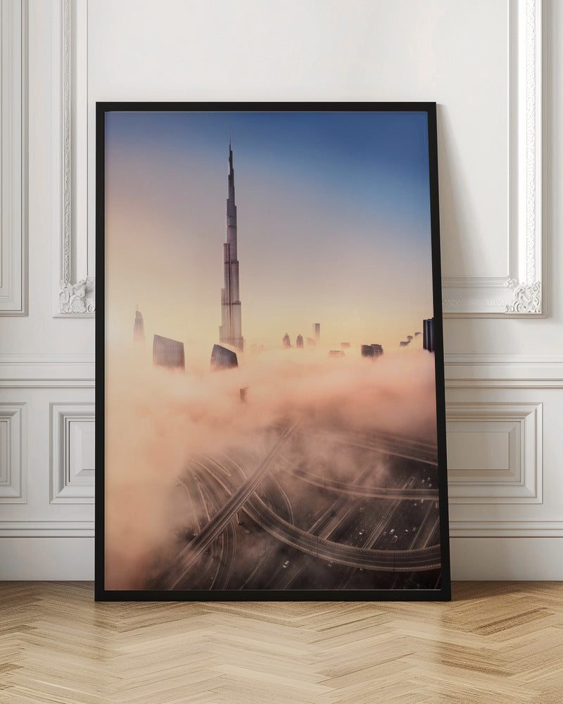 An aerial photograph of the Burj Khalifa in Dubai, towering over a thick blanket of pink and orange-hued fog at sunrise. Below the fog, a complex highway interchange is visible, with the clear blue sky above. Wall Art