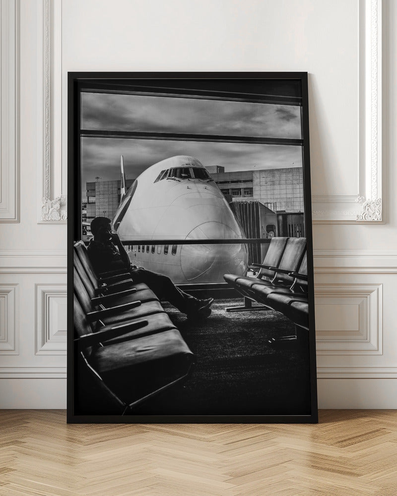 A dramatic black and white photograph of a silhouetted person sitting in an airport departure lounge, waiting for their flight. Through the large window, the enormous nose of a Boeing 747 jumbo jet is visible up close, dominating the view under a cloudy sky. Artwork