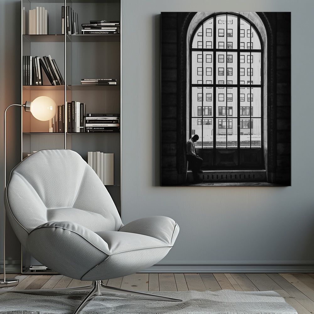 A black and white photograph of a solitary man sitting with his head bowed on the ledge of a massive arched window. The window's dark mullions create a grid over the bright view of another building outside, while the man remains in the shadows, creating a pensive and lonely mood. Poster