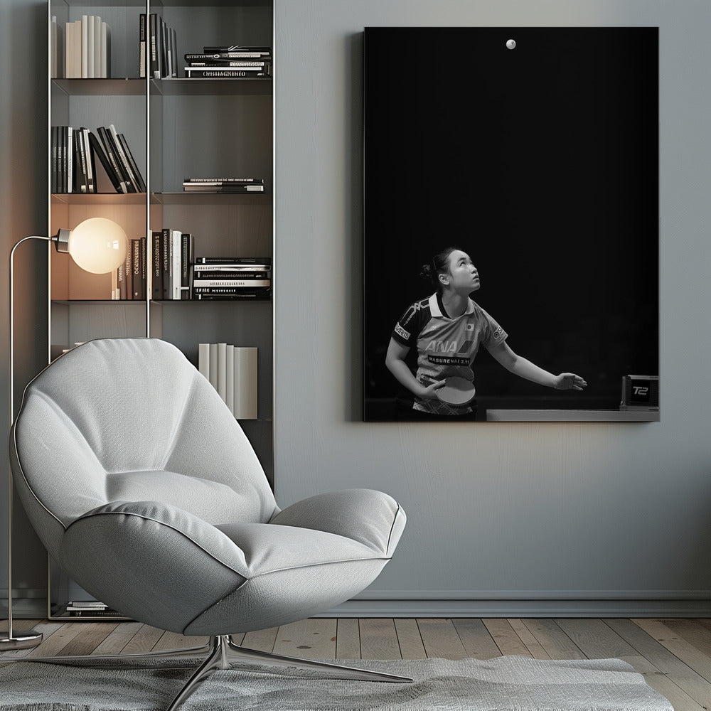 A dramatic black and white vertical photograph of a female table tennis player mid-serve. Positioned in the lower-left, she looks up with intense focus at the white ball suspended high in the air against a solid black background. Poster