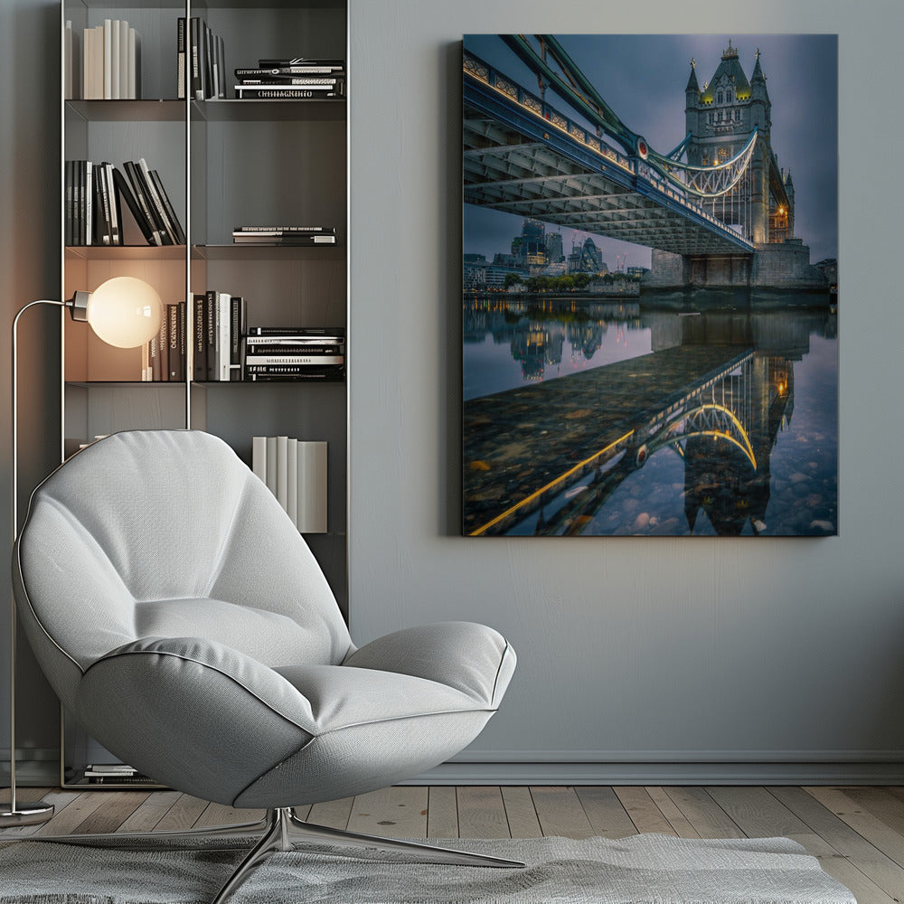 A dramatic, low-angle photograph of London's Tower Bridge at dusk. The iconic bridge is illuminated with warm yellow lights against a dark blue, cloudy sky. The calm River Thames in the foreground creates a stunning, clear reflection of the bridge and the distant city skyline. Print