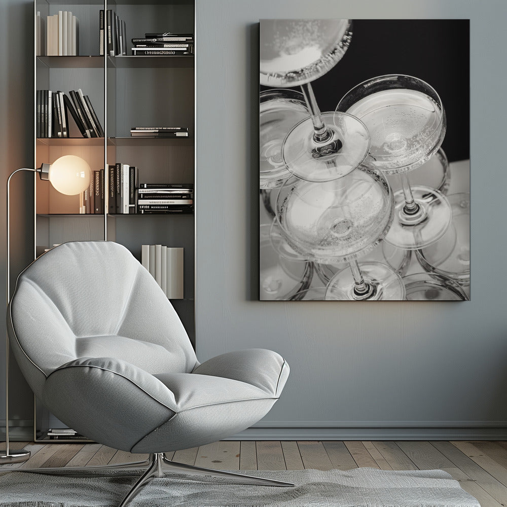 A close-up, high-angle photograph in black and white of a champagne tower. Several coupe-style glasses are stacked, filled with bubbly champagne that catches the light. The background is dark, creating a strong contrast and highlighting the elegant glassware. Decor