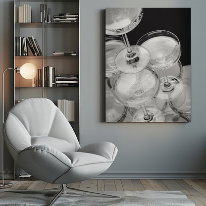 A close-up, high-angle photograph in black and white of a champagne tower. Several coupe-style glasses are stacked, filled with bubbly champagne that catches the light. The background is dark, creating a strong contrast and highlighting the elegant glassware. Decor