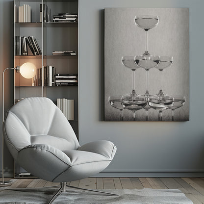 A classic black and white photograph of a champagne tower, with coupe glasses stacked in a pyramid. The glasses are filled with bubbly liquid, and the composition is set against a textured light gray background and enclosed in a black frame. Poster