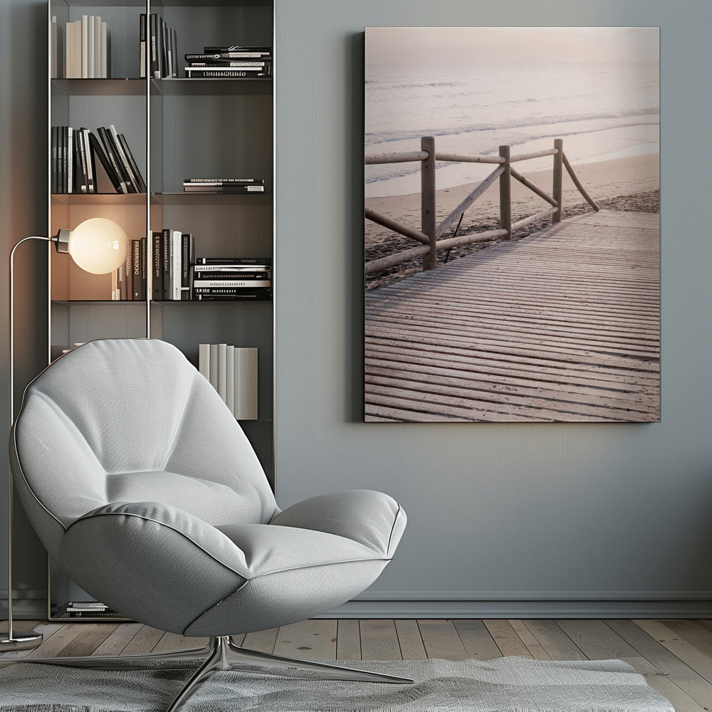 A wooden boardwalk with a rustic log fence leads down to a sandy beach with gentle waves lapping at the shore under a soft, hazy sunrise or sunset. Decor