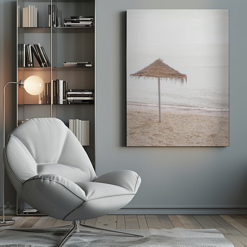 A minimalist photograph of a solitary thatched umbrella on a sandy beach, with calm, grey water and a hazy, overcast sky in the background, creating a serene and tranquil coastal scene. Poster