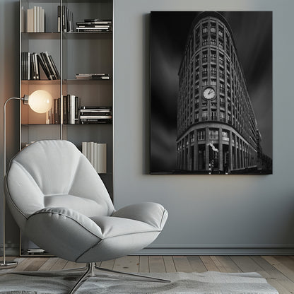 A dramatic low-angle, black and white photograph of a large, curved corner building with a prominent clock on its facade. The sky is dark with a motion blur effect, making the building appear grand and imposing. Artwork