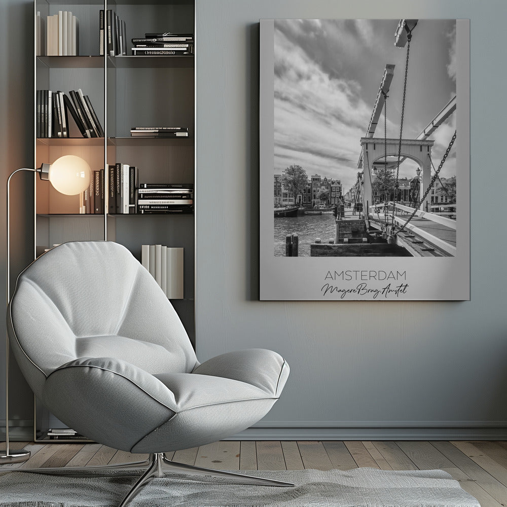A black and white travel poster of Amsterdam, featuring a side view of the Magere Brug, a traditional wooden drawbridge, over the Amstel river. Classic canal houses line the waterway in the background under a dramatic, cloudy sky. The image is in a black frame and has text at the bottom that reads 'AMSTERDAM', 'Magere Brug, Amstel', and 'NEDERLAND'. Artwork