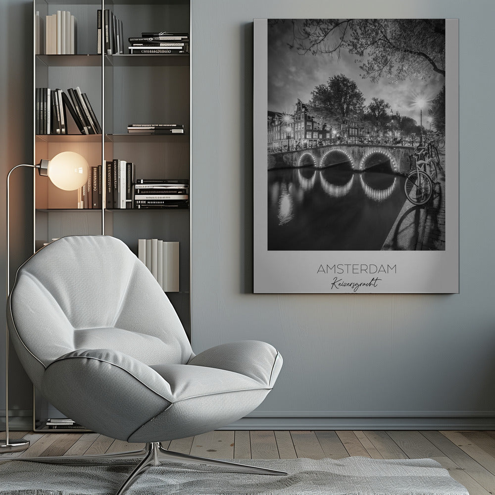 A black and white poster of Amsterdam's Keizersgracht canal at night. An arched bridge with glowing lights is the centerpiece, its reflection shimmering on the dark water. Bicycles are parked along the bridge and in the foreground on a cobblestone path. Classic canal houses and trees line the background under a dramatic, cloudy sky. The image is framed with text below reading 'AMSTERDAM Keizersgracht NEDERLAND'. Artwork