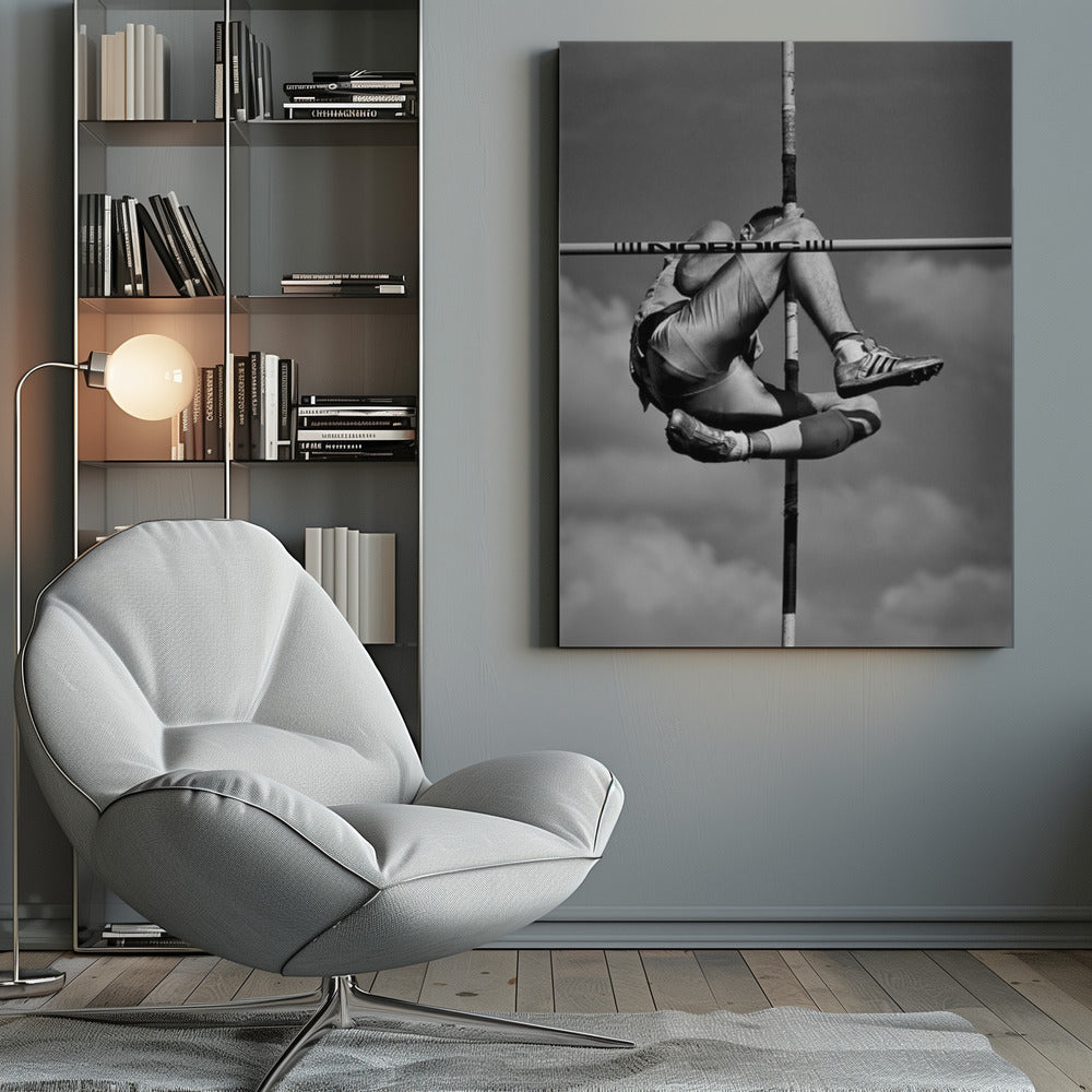 A dramatic black and white, low-angle photograph of a male athlete in mid-air during a pole vault. He is arching his back and bending his legs to clear the horizontal bar, with the vertical pole bisecting the frame. The background is a partly cloudy sky. Wall Art