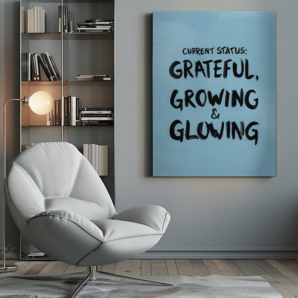 A motivational poster with a light blue background and a thin black frame. The text 'CURRENT STATUS: GRATEFUL, GROWING & GLOWING' is written in a bold, black, handwritten brush font. Decor