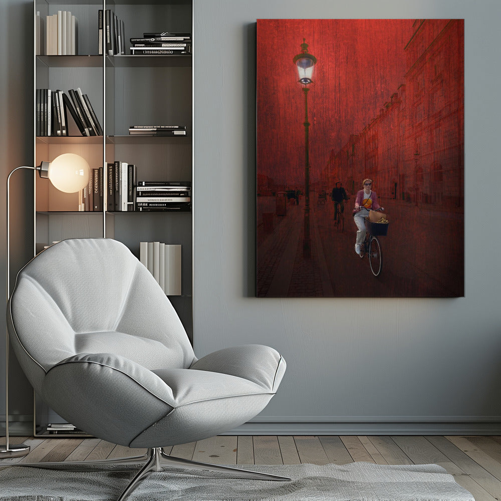 A surreal artistic image of a city street bathed in a textured red light. A woman rides a bicycle with a basket towards the viewer, while another cyclist is in the background. A tall, ornate lamppost is lit on the left side of the cobblestone street. Wall Art
