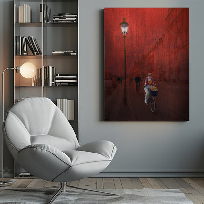 A surreal artistic image of a city street bathed in a textured red light. A woman rides a bicycle with a basket towards the viewer, while another cyclist is in the background. A tall, ornate lamppost is lit on the left side of the cobblestone street. Wall Art