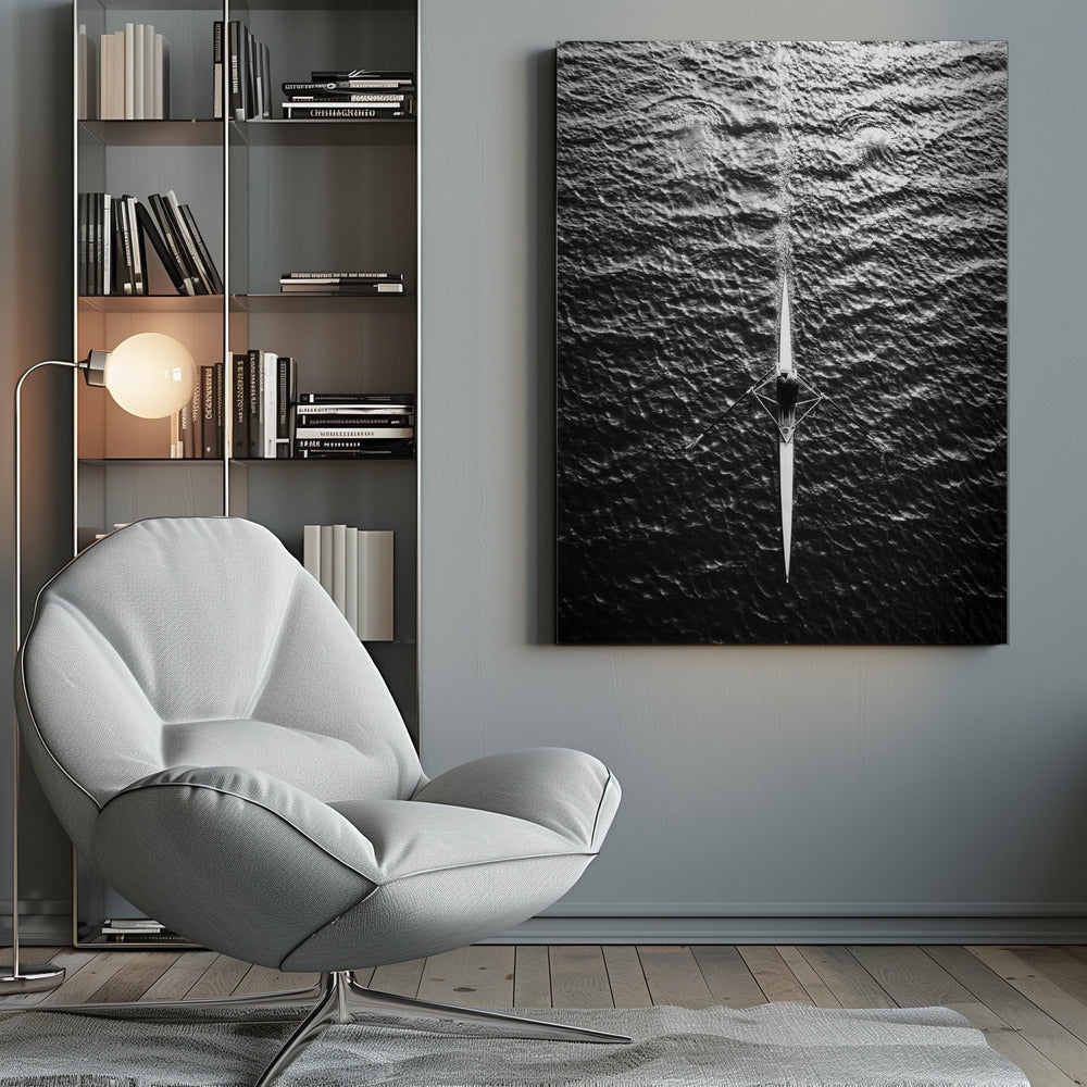 A dramatic black and white overhead photograph of a lone rower in a sleek racing shell, cutting a straight path through dark, textured water. The high-contrast lighting highlights the ripples on the water's surface and the rower's focused form. Artwork