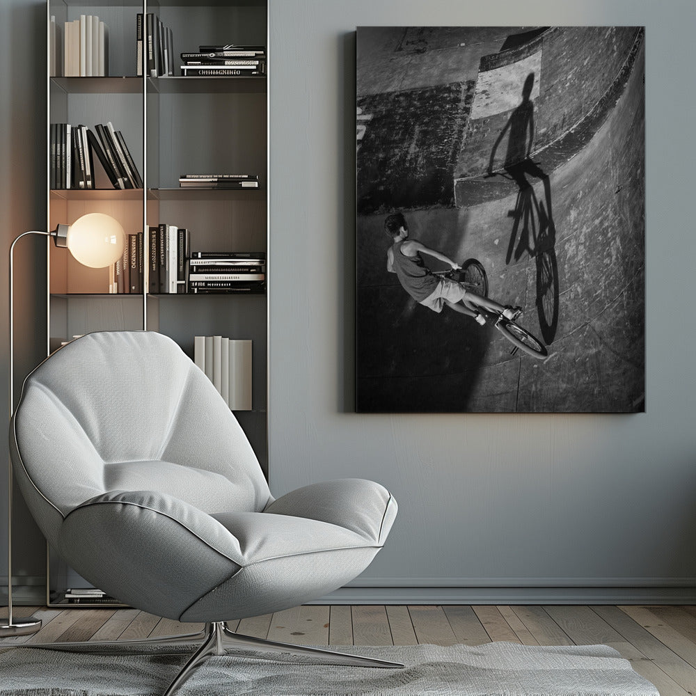 A dramatic black and white high-angle photograph of a BMX rider in a skate park. The rider is captured in motion on a curved ramp, while their long, stark shadow is cast on the worn, textured surface ahead, creating a powerful visual contrast. Poster