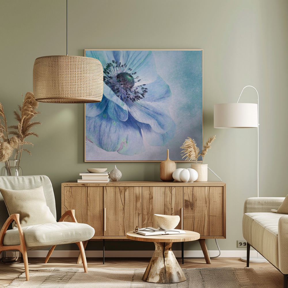 A close-up, artistic photograph of a large blue anemone flower with delicate, layered petals. The center of the flower is a dark, textured black and purple. The background is a soft, textured light blue. The entire image is enclosed in a light-colored wooden frame. Decor