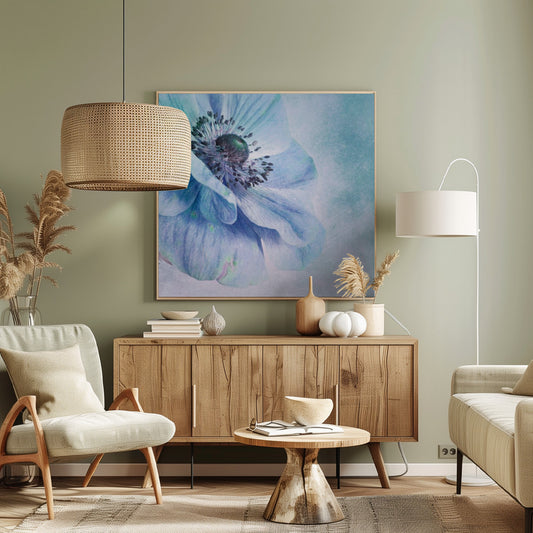 A close-up, artistic photograph of a large blue anemone flower with delicate, layered petals. The center of the flower is a dark, textured black and purple. The background is a soft, textured light blue. The entire image is enclosed in a light-colored wooden frame. Decor