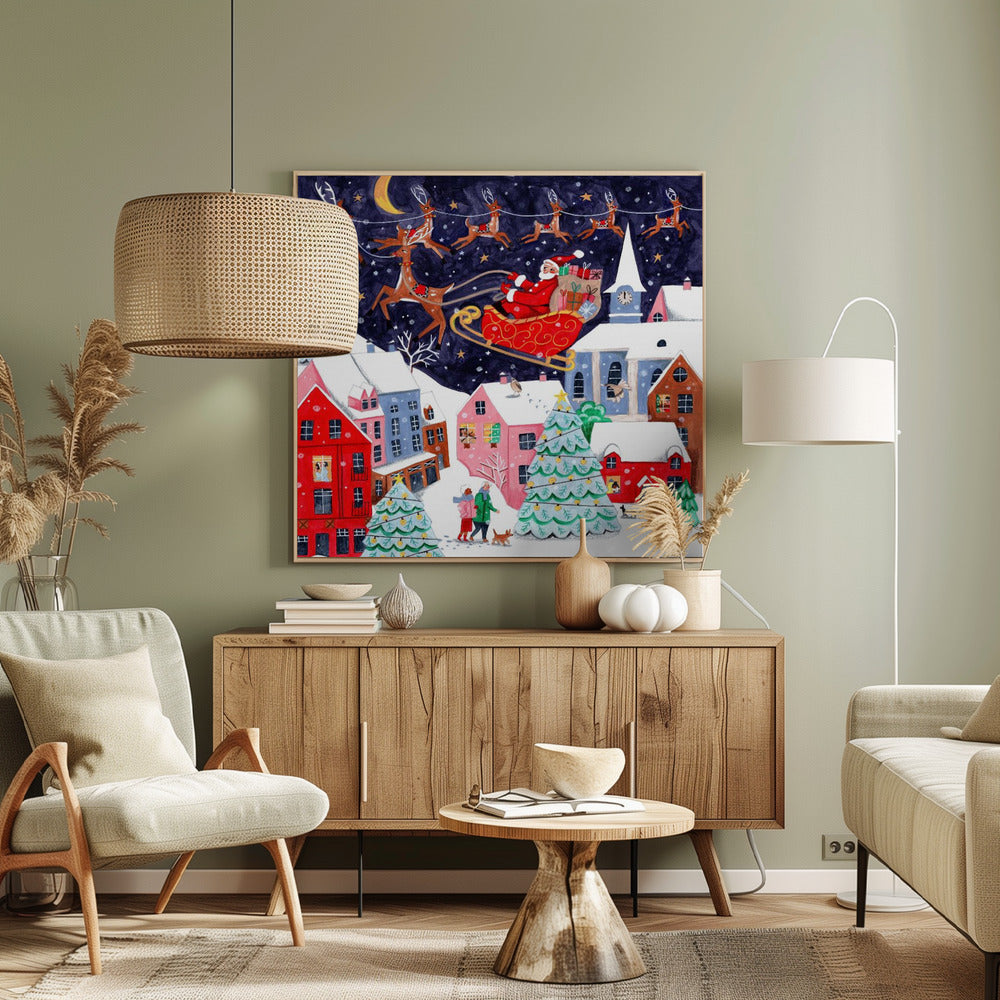 A festive illustration of Santa Claus flying in his sleigh pulled by reindeer over a snowy European-style village at night. The sky is a deep starry blue with a crescent moon, and the houses below are painted in vibrant reds, pinks, and blues, with warm light in the windows. People walk in the snow near decorated Christmas trees. Decor