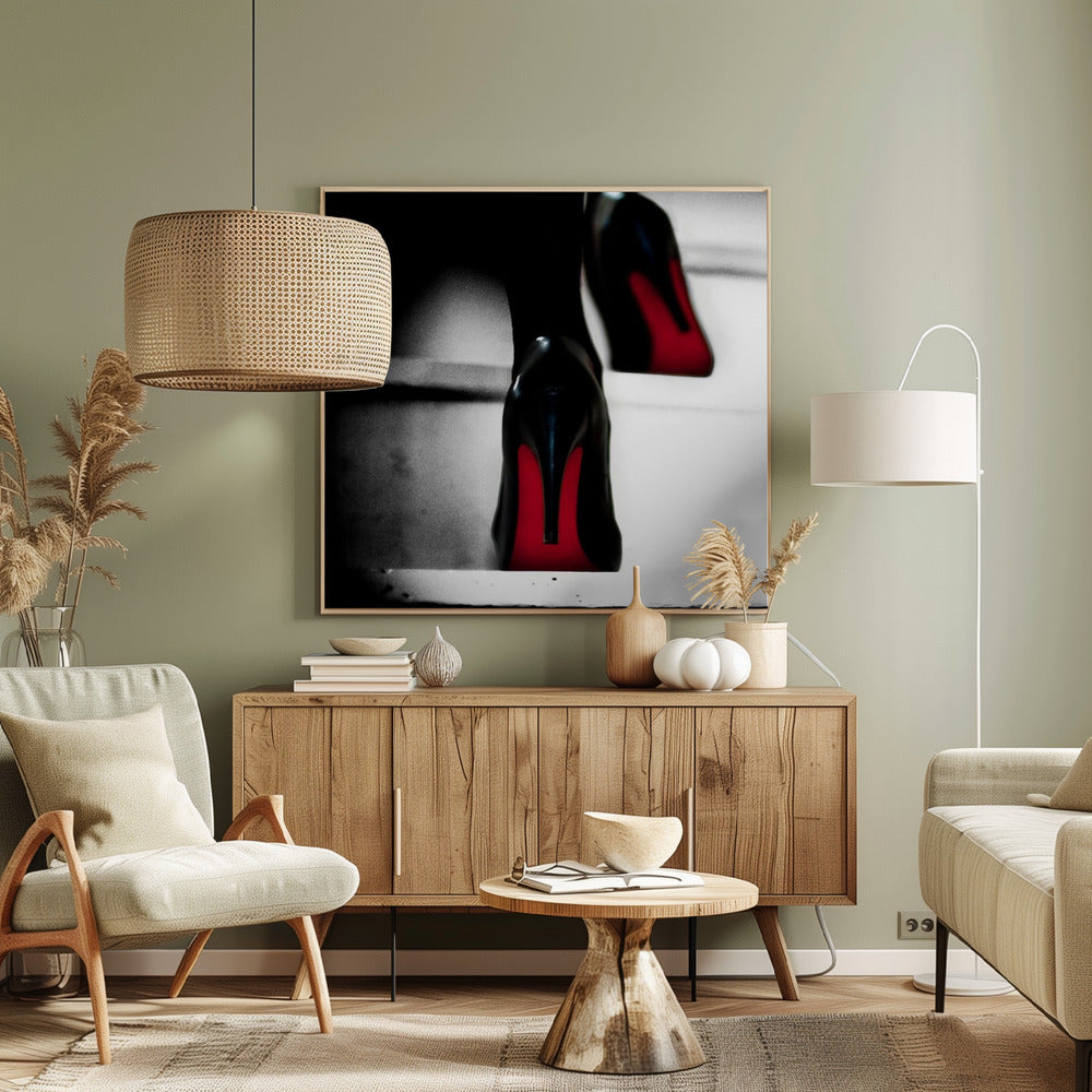 A dramatic, low-angle, black and white photograph focusing on the back of a person wearing glossy black high heels with vibrant red soles, all set within a light wood frame. Artwork