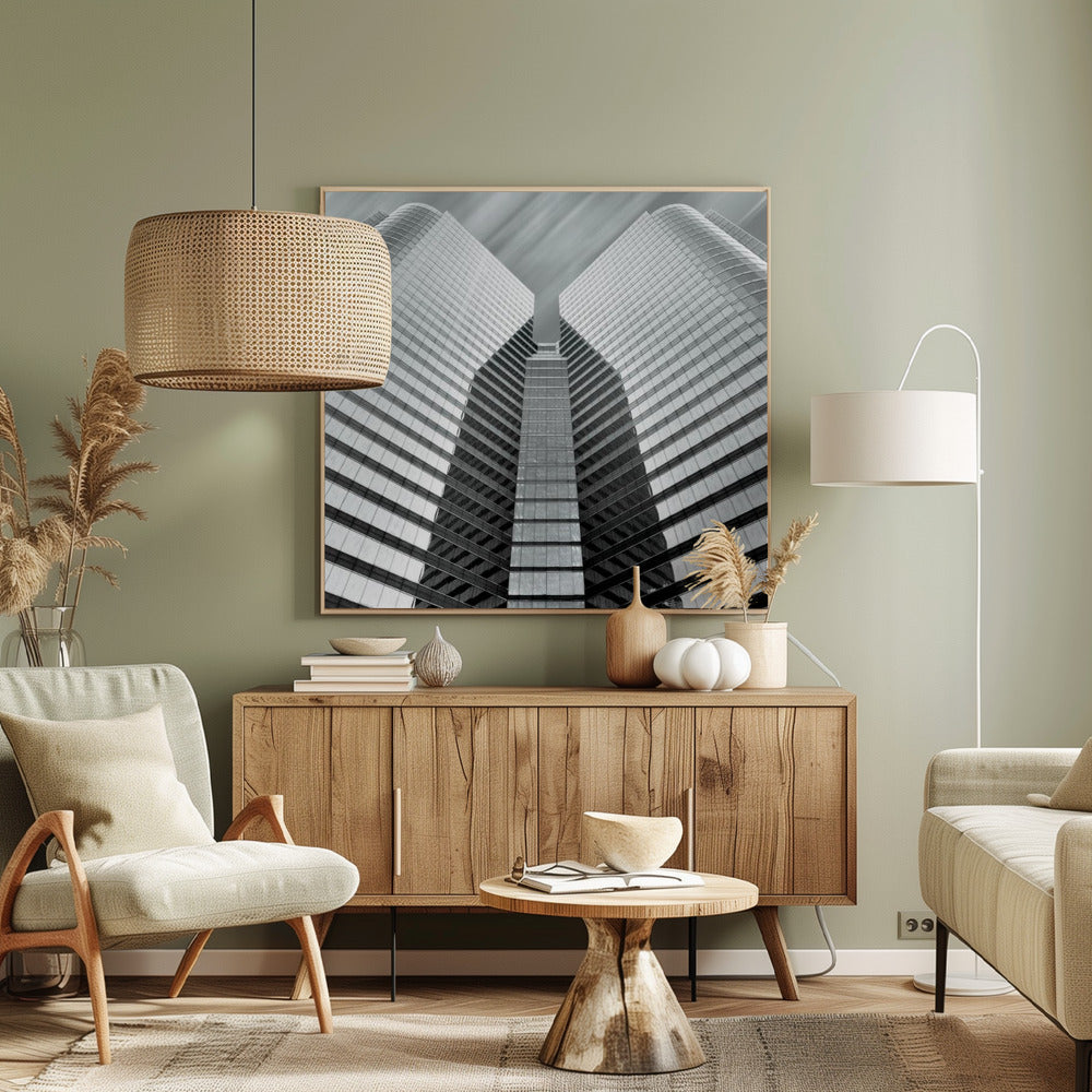A low-angle, symmetrical black and white photograph of a modern glass skyscraper. The two towers of the building converge towards the center, creating a V-shape against a sky with motion-blurred clouds. The photo is enclosed in a light-colored wooden frame. Print
