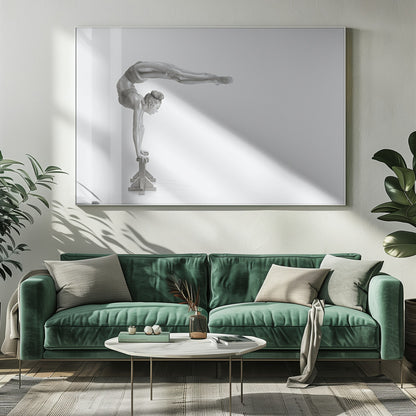 A framed black and white photograph of a female gymnast with a metallic silver-painted body, balancing in a difficult handstand pose on small blocks against a stark white background. Her back is arched and her legs are extended straight out behind her, parallel to the ground. Artwork