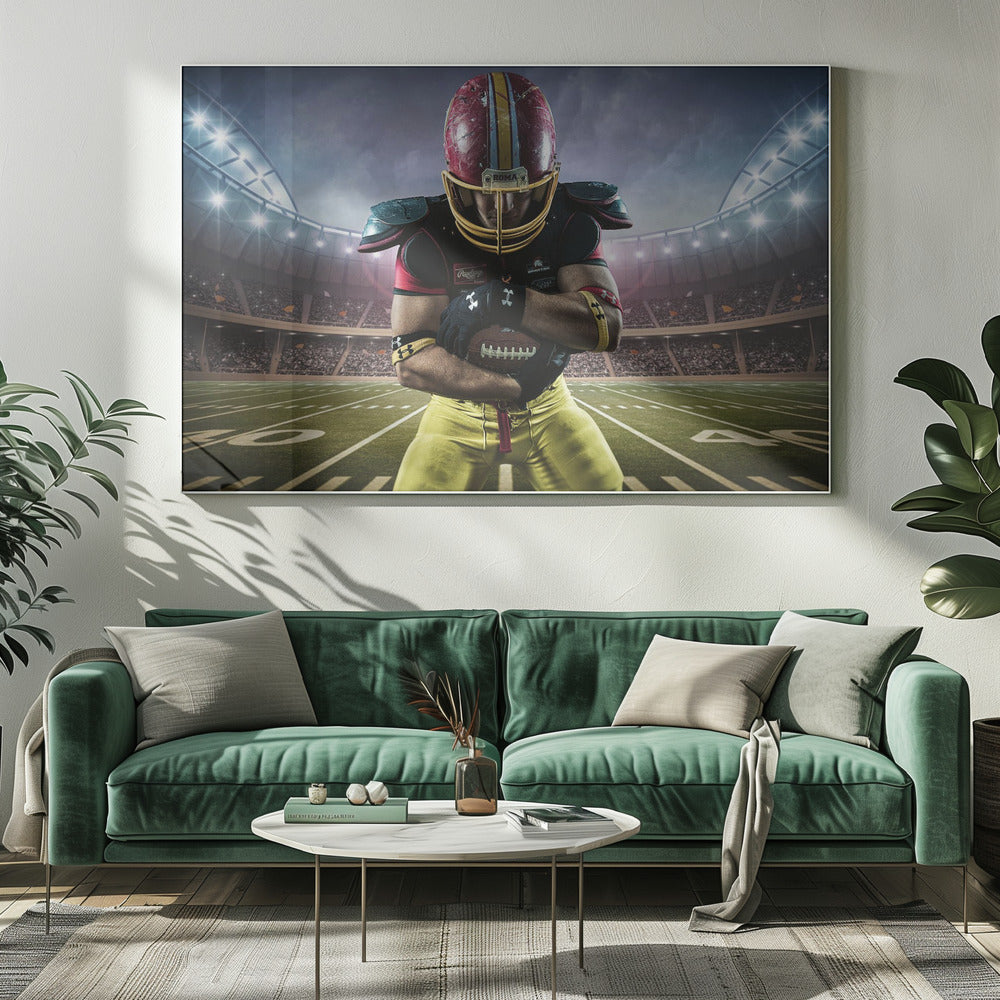 A framed poster of a determined football player in a red and yellow uniform standing on a field in a packed stadium. He is holding a football close to his chest with his head bowed, under bright stadium lights. Decor