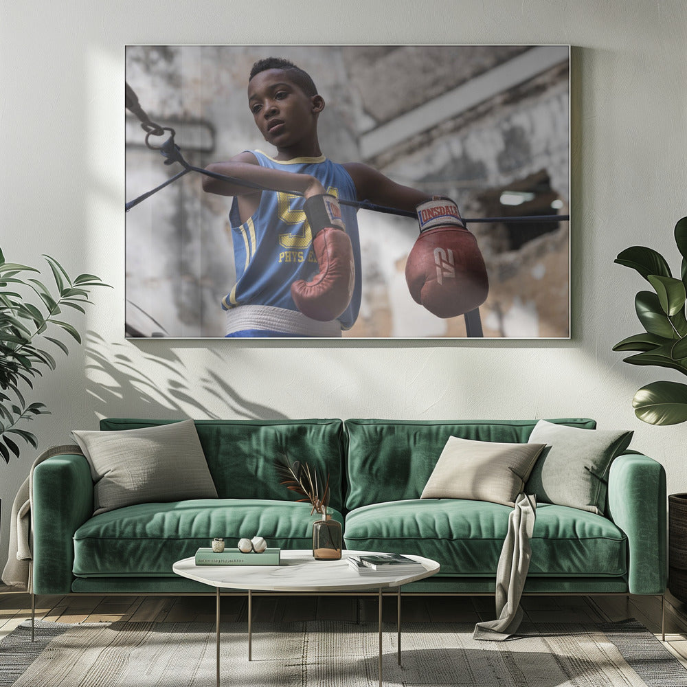 A young Black boy in a blue jersey and red boxing gloves leans pensively against the ropes of a boxing ring, looking away with a thoughtful expression against a blurred, weathered background. Wall Art