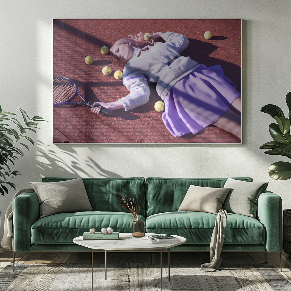 A high-angle shot of a young woman with pink hair lying on a red clay tennis court, surrounded by yellow tennis balls. She wears a grey sweater, a white collared shirt, and a purple pleated skirt, and holds a tennis racket in one hand. The scene is framed with a silver border. Wall Art