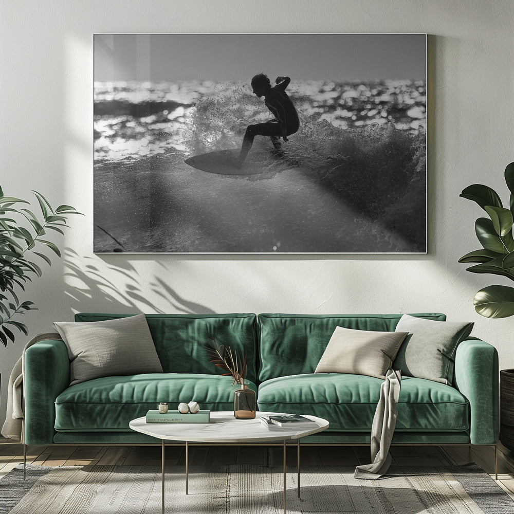 A black and white action shot of a surfer silhouetted against the sparkling ocean. The surfer is crouched low on their board, carving through a wave and creating a dramatic spray of water. The photo is enclosed in a silver frame. Print