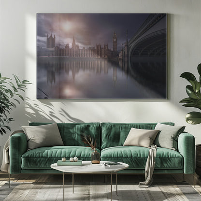 A dramatic, atmospheric photograph of the Houses of Parliament and Big Ben in London, reflected in the still waters of the River Thames. A bright sun breaks through dark, moody clouds, casting a warm light on the scene, with a stone bridge visible to the right. The image is enclosed in a silver frame. Print