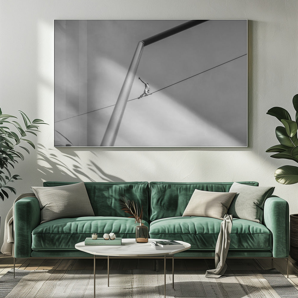 A black and white, low-angle photograph of a person balancing while sitting on a tightrope high in the sky. A large metal pole is in the foreground, creating a strong diagonal line. The image is framed in silver. Decor