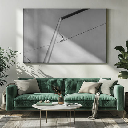 A black and white, low-angle photograph of a person balancing while sitting on a tightrope high in the sky. A large metal pole is in the foreground, creating a strong diagonal line. The image is framed in silver. Decor